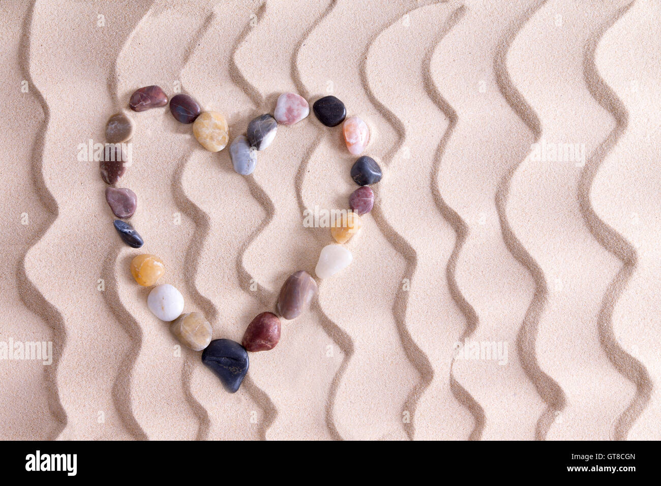 Dekorative Kiesel Herz Fersenone alluvialen Quarzit, Achat und Basalt Steine symbolisch für Liebe und Romantik am goldenen Strand Stockfoto