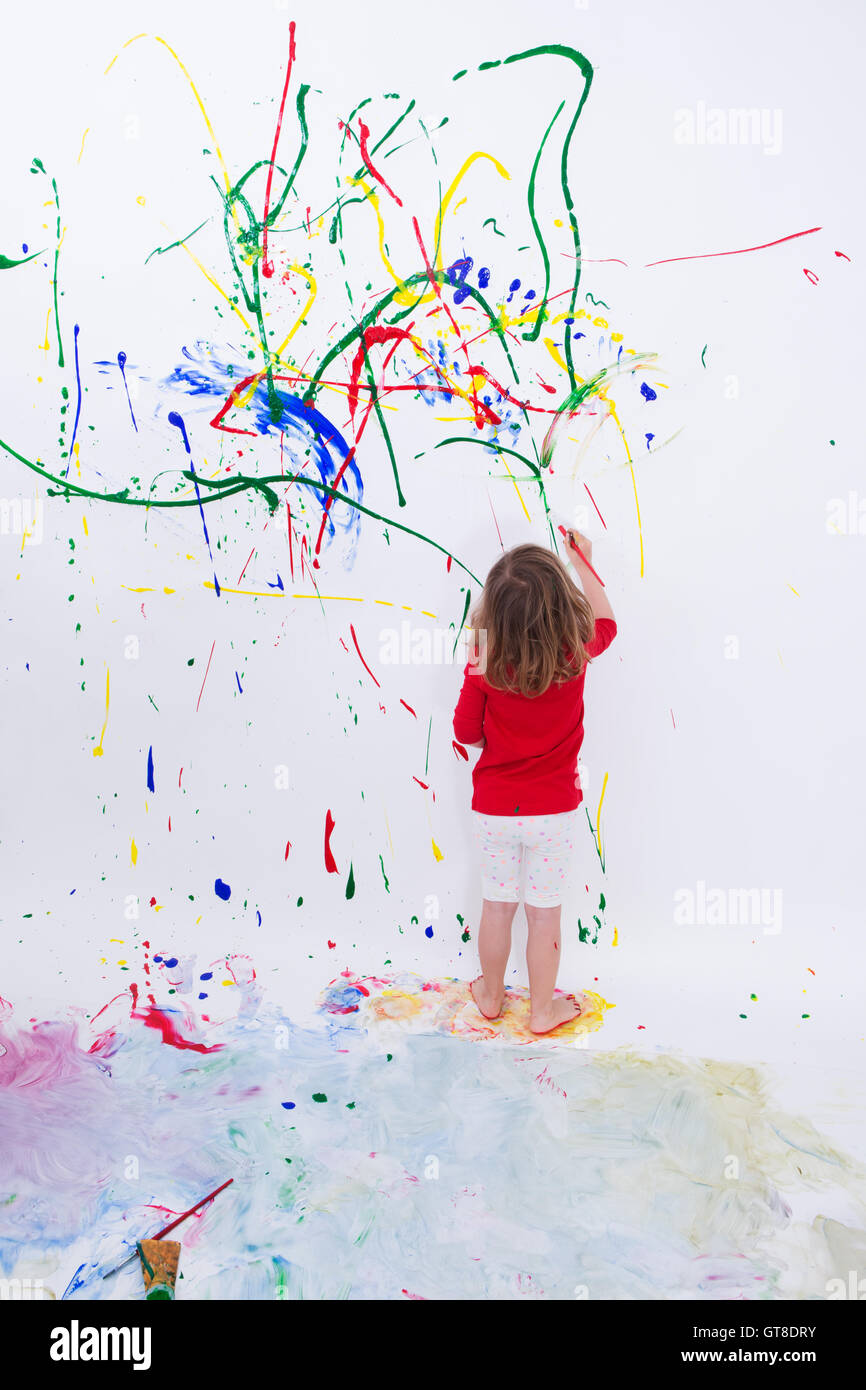 Voller Länge geschossen eines jungen kleinen Kind Malerei etwas abstrakt auf weißen großen Wand mit unterschiedlichen Farben. Stockfoto