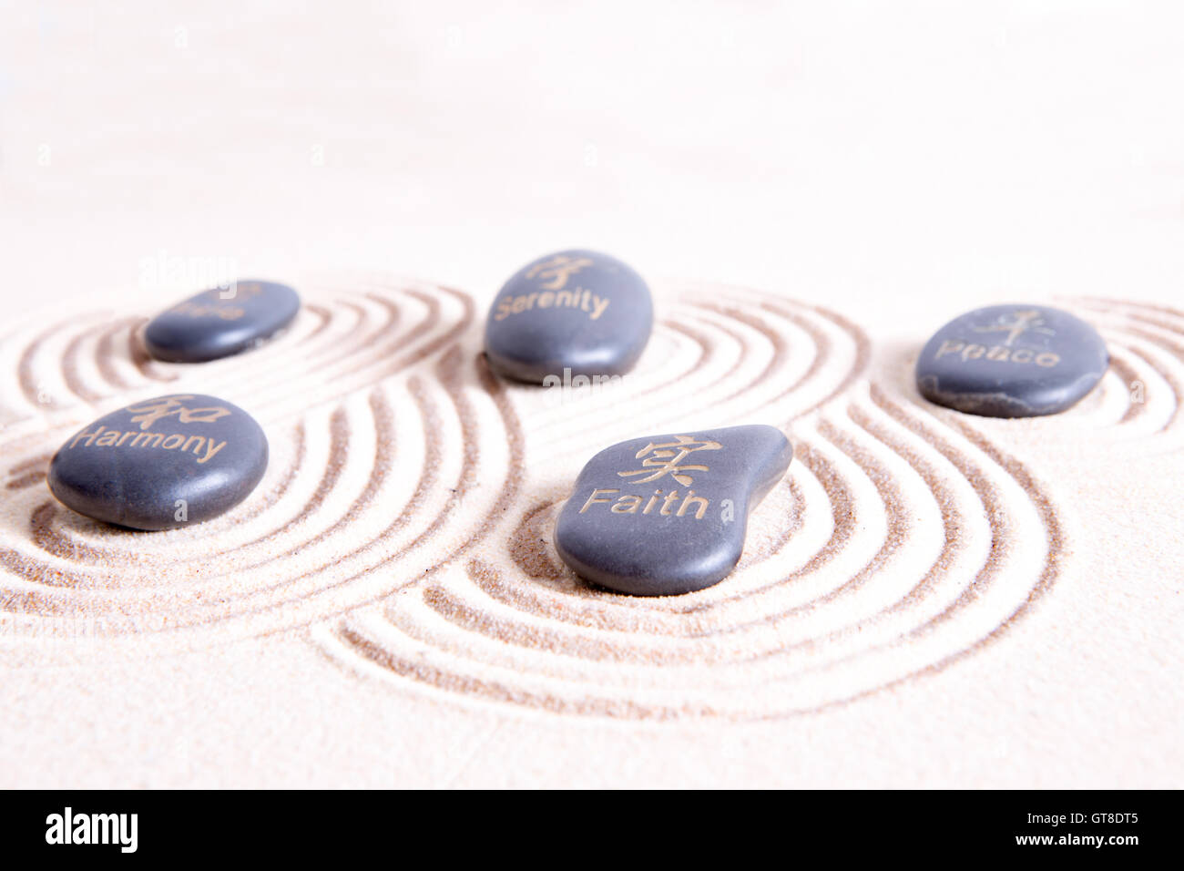 Zen-Kunst mit wirbelnden Linien im goldenen Sand rund um glatte Basalt Felsen mit Symbolen und Text bedeutet Frieden, Harmonie, Hoffnung Stockfoto