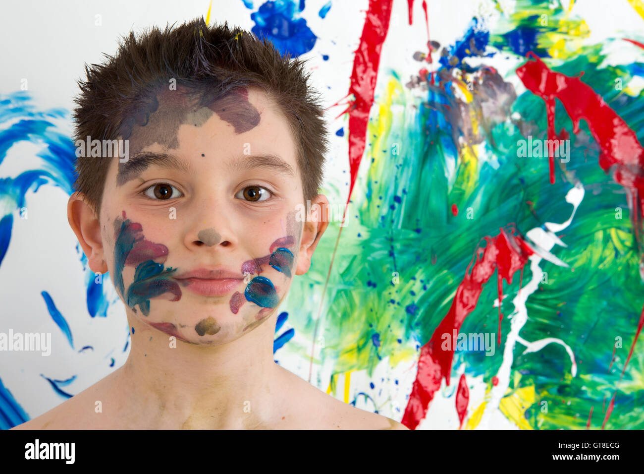 Hübscher Junge mit bunten Farben überall auf seinem Gesicht stand vor seiner neuen moderne abstrakte Kunstwerke mit einem Blen beschmiert Stockfoto