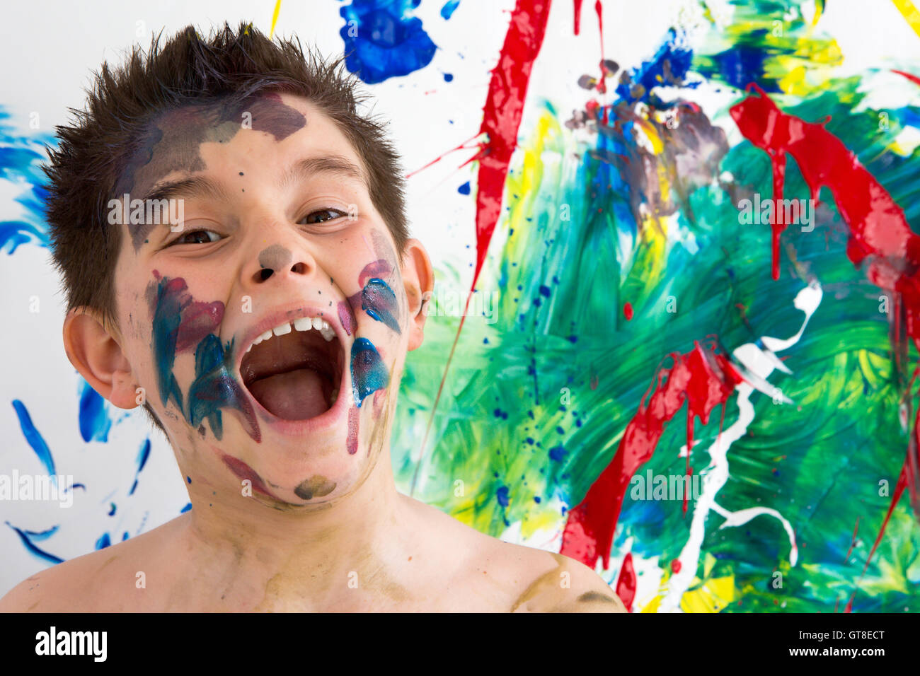 Lustige künstlerischen kleiner Junge mit Farbe Steinpyramiden auf seinem Gesicht stand vor seinem abgeschlossenen moderne abstrakte Schöpfung Lachen ein Stockfoto