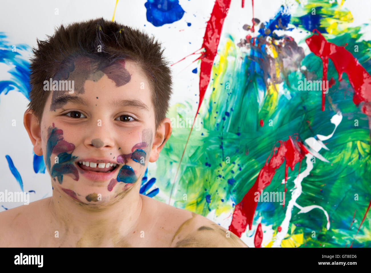 Glücklich kreativen kleinen Jungen mit Farbe Steinpyramiden auf seinem Gesicht stand vor seiner leuchtend bunte moderne abstrakte Malerei Grinsen Stockfoto