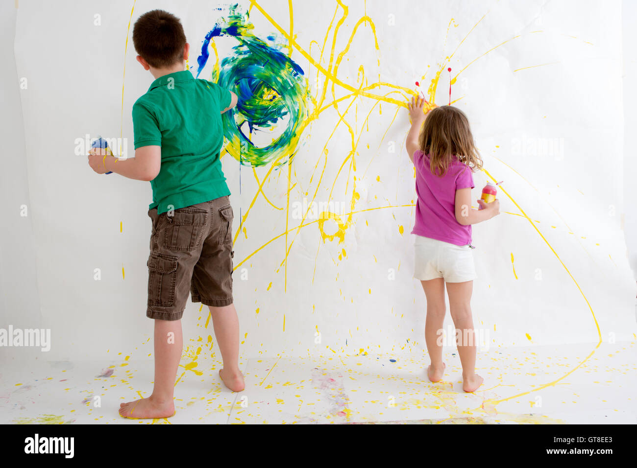 Zwei kleine Kinder, ein zehn Jahre alter Junge und drei Einjahresmädchen, malt Freihandzeichnung an einer Wand mit bunten Acryl creatin Stockfoto