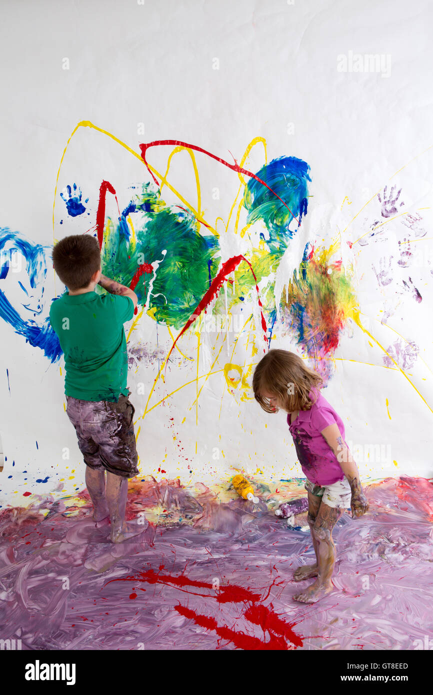 Junger Bruder und Schwester malen gemeinsam schaffen eine moderne abstrakte von lebendigen Farben an der Wand und Boden mit ihren imaginat Stockfoto