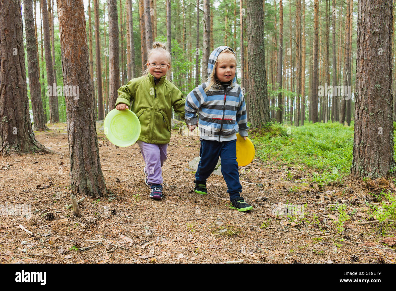 4 Jahre alten Bruder und Schwester zu Fuß mit ihren Frisbees durch den Wald, Schweden Stockfoto
