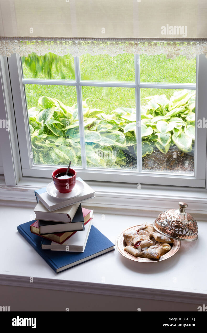 Tasse heißen schwarzen Kaffee auf gestapelten Bücher und Teller mit leckeren Blätterteige auf die Glasfenster für die Lesezeit mit Snacks-Konzept Stockfoto