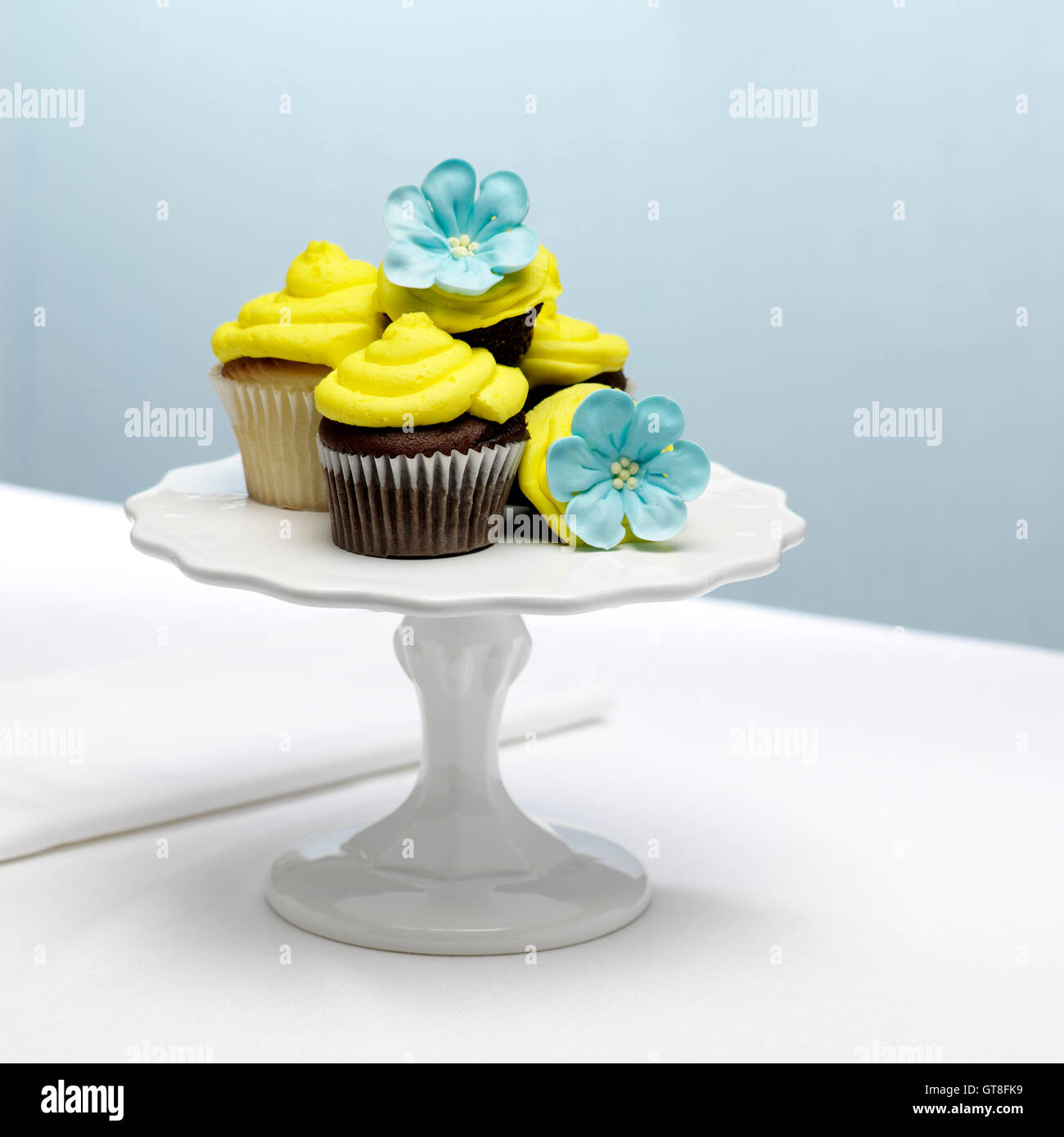 Schokolade und Vanille Cupcakes mit gelber Glasur und blauer Zucker Blumen auf Kuchen stehen Stockfoto