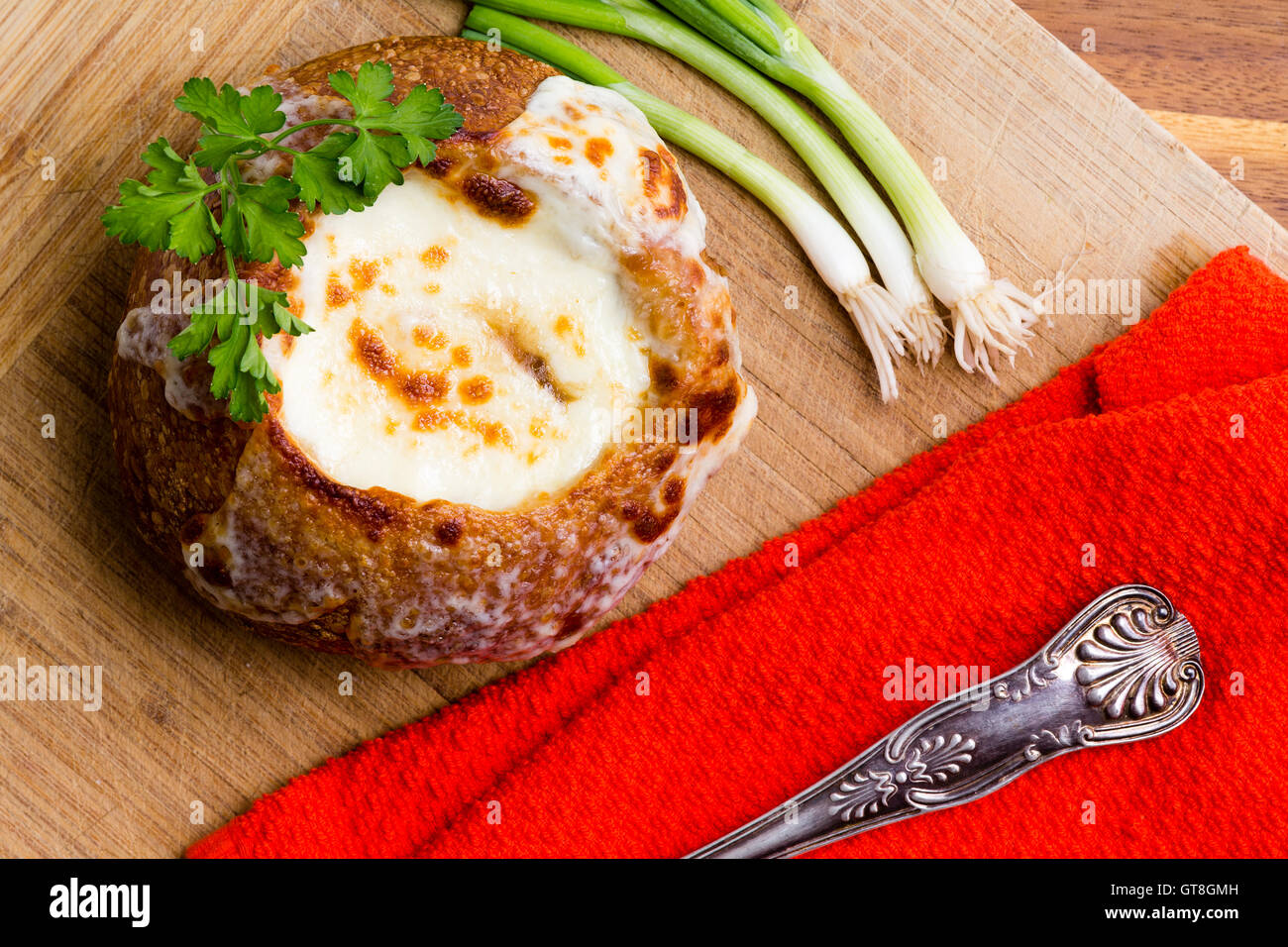 Leckere heiße cremige Zwiebelsuppe serviert in einer Brotschale garniert mit frischer Petersilie mit einem bunten roten Serviette und frischen spri Stockfoto