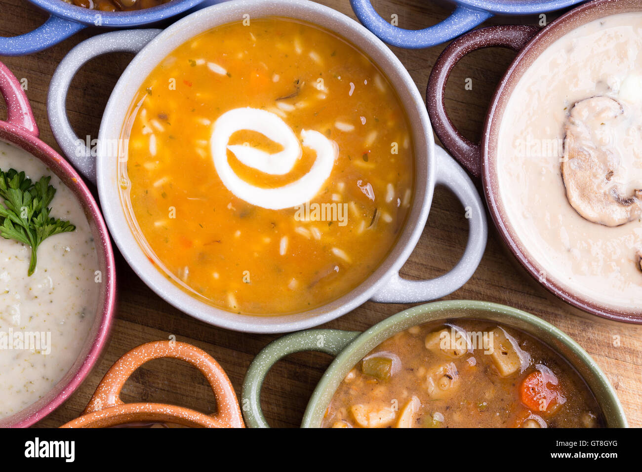 Draufsicht der sortierten Suppe in Schalen mit Griffen mit Fokus auf eine Tasse Hühnerbrühe mit wildem Reis garniert mit einem Strudel Stockfoto