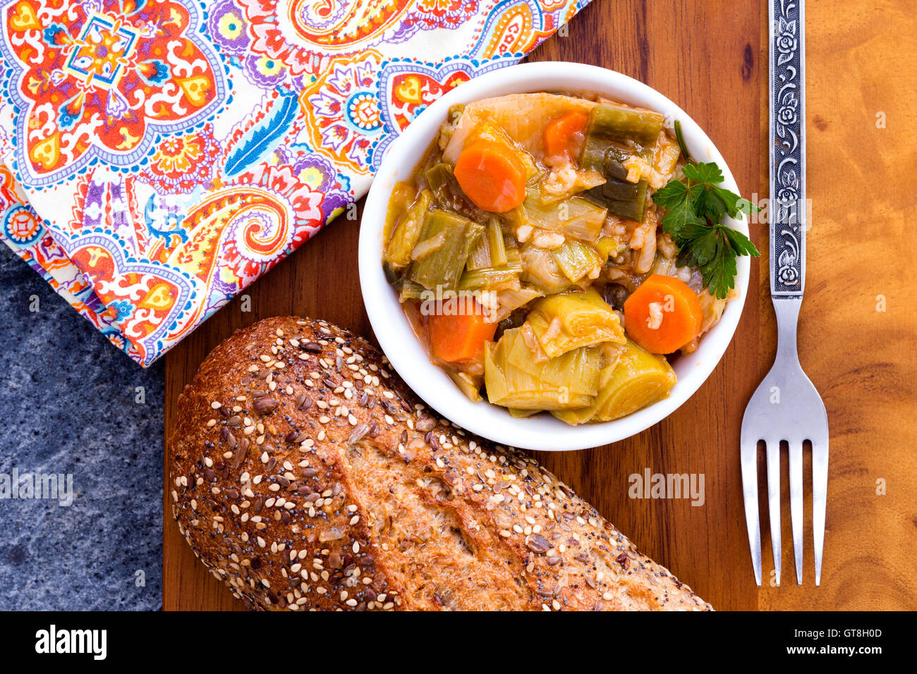 Schale mit leckeren hausgemachten Lauch und Karotten Eintopf in der Küche auf einem Holzbrett serviert, mit einer Gabel und bunte Serviette, Stockfoto