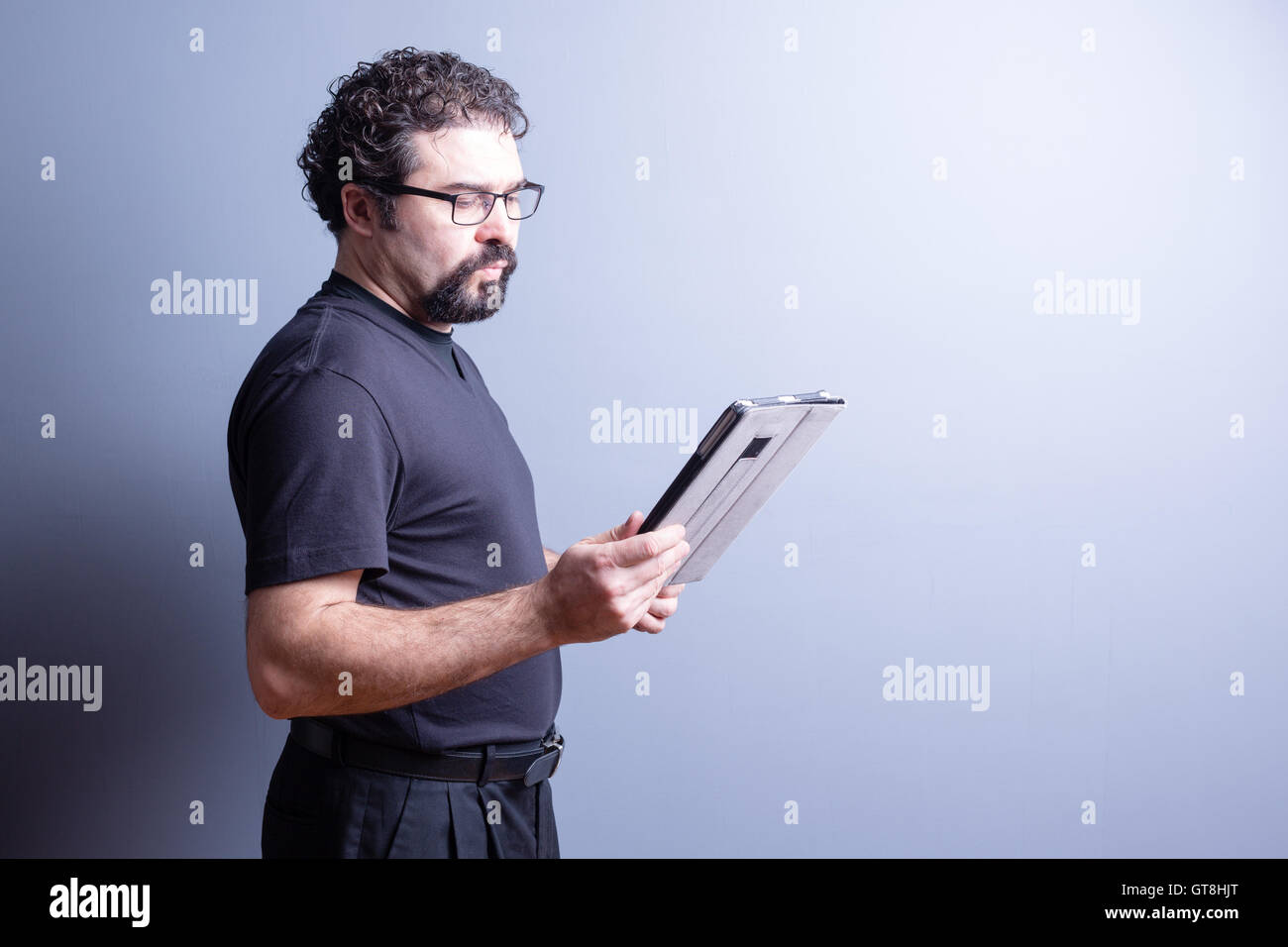 Profil von Mann mit T-Shirt und Brille suchen seriöse und Lesen von Tablet-Computer im Studio mit grauem Hintergrund, S Stockfoto