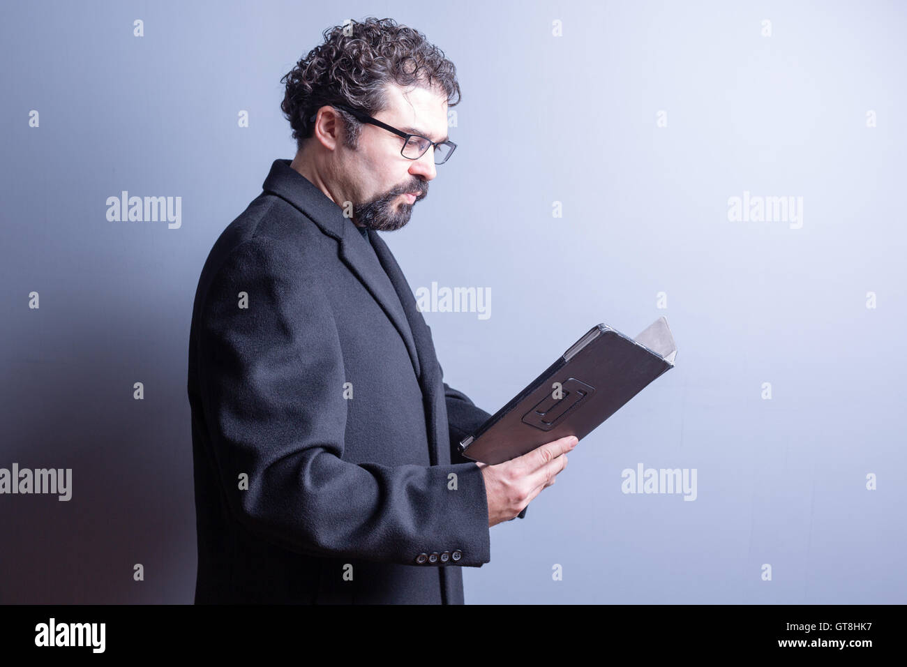 Taille bis Business Mann tragen Jackett und Brille suchen ernsthafte während Lesung Computer Tablet im Studio mit grauen Ba Stockfoto