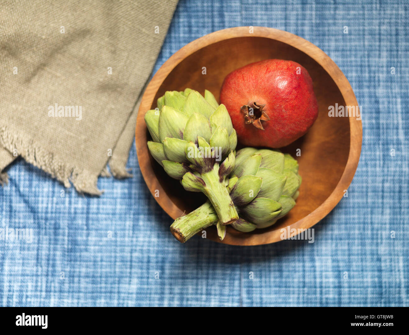 Draufsicht der Granatapfel und Artischocken in Holzschale auf Blaue Tischdecke Stockfoto