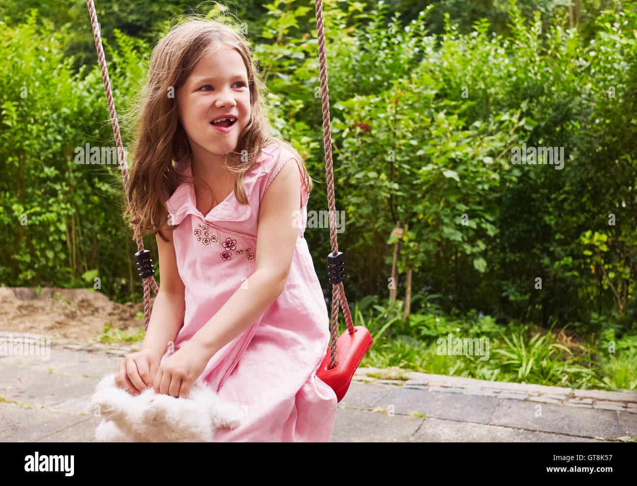 5 Jahre altes Mädchen sitzt auf einer Schaukel im Garten, Deutschland Stockfoto