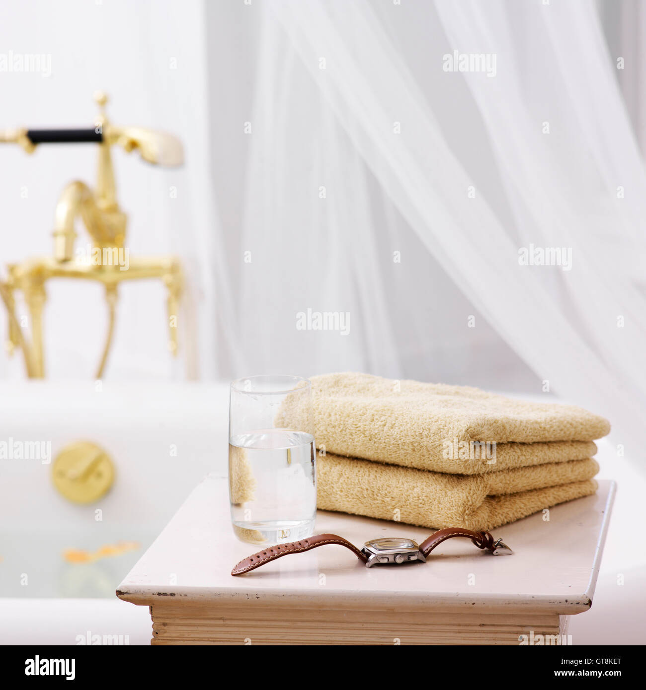 Beistelltisch im Badezimmer mit Handtüchern, Glas Wasser und Uhr Stockfoto
