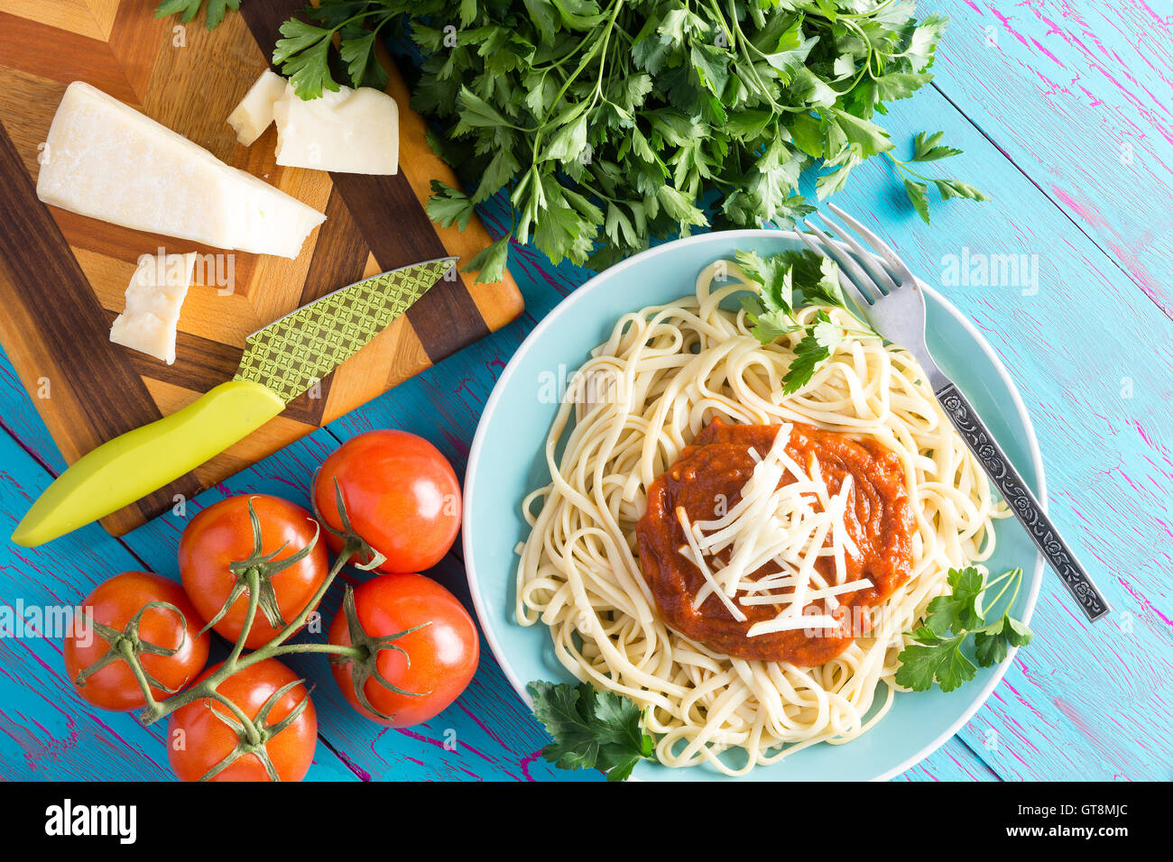 Blick von oben auf Runde Teller mit frisch zubereiteten Spaghetti mit roter Soße, Petersilie und Greyerzer Käse neben Messer gekrönt Stockfoto