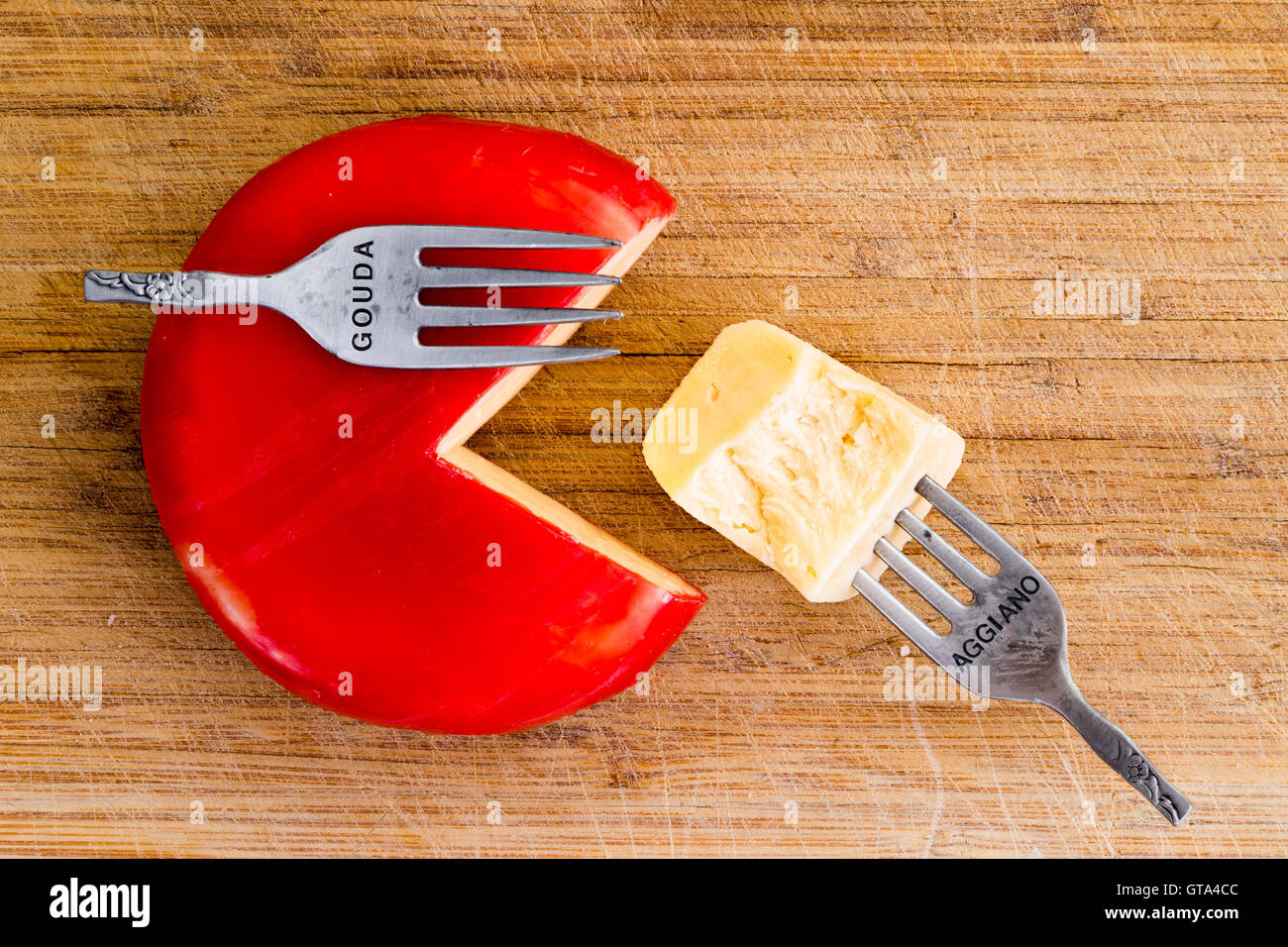 Kreative Anordnung von Wachs bedeckt Käse Rad mit einem Viertel schneiden und einer Gabel mit Käse Stück platziert, als ob Fütterung Stockfoto