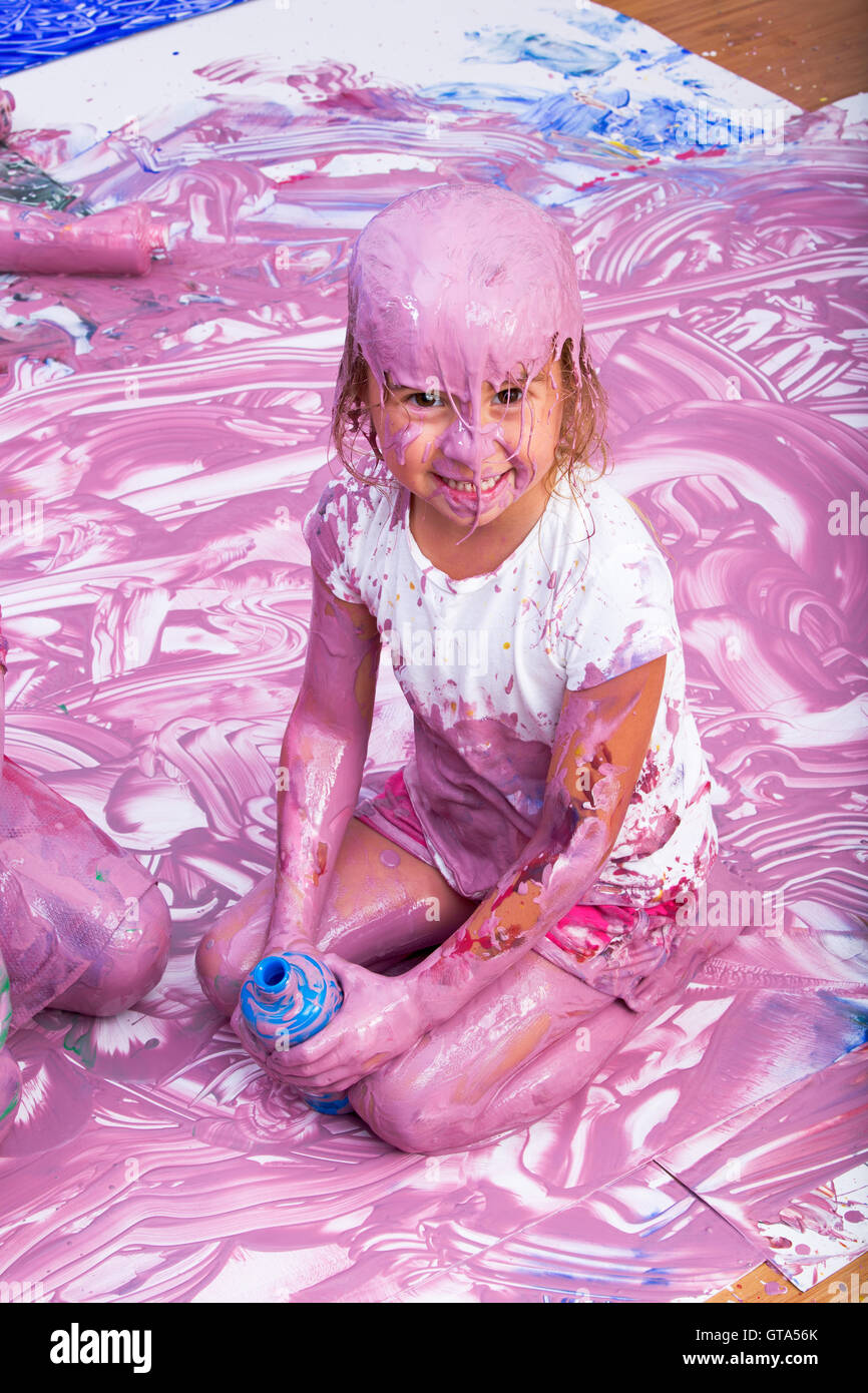 Lachen niedliche Mädchen Holding leere Flasche während klatschnass in rosa Farbe von Kopf bis Fuß. Sie sitzt in der Mitte des großen canva Stockfoto