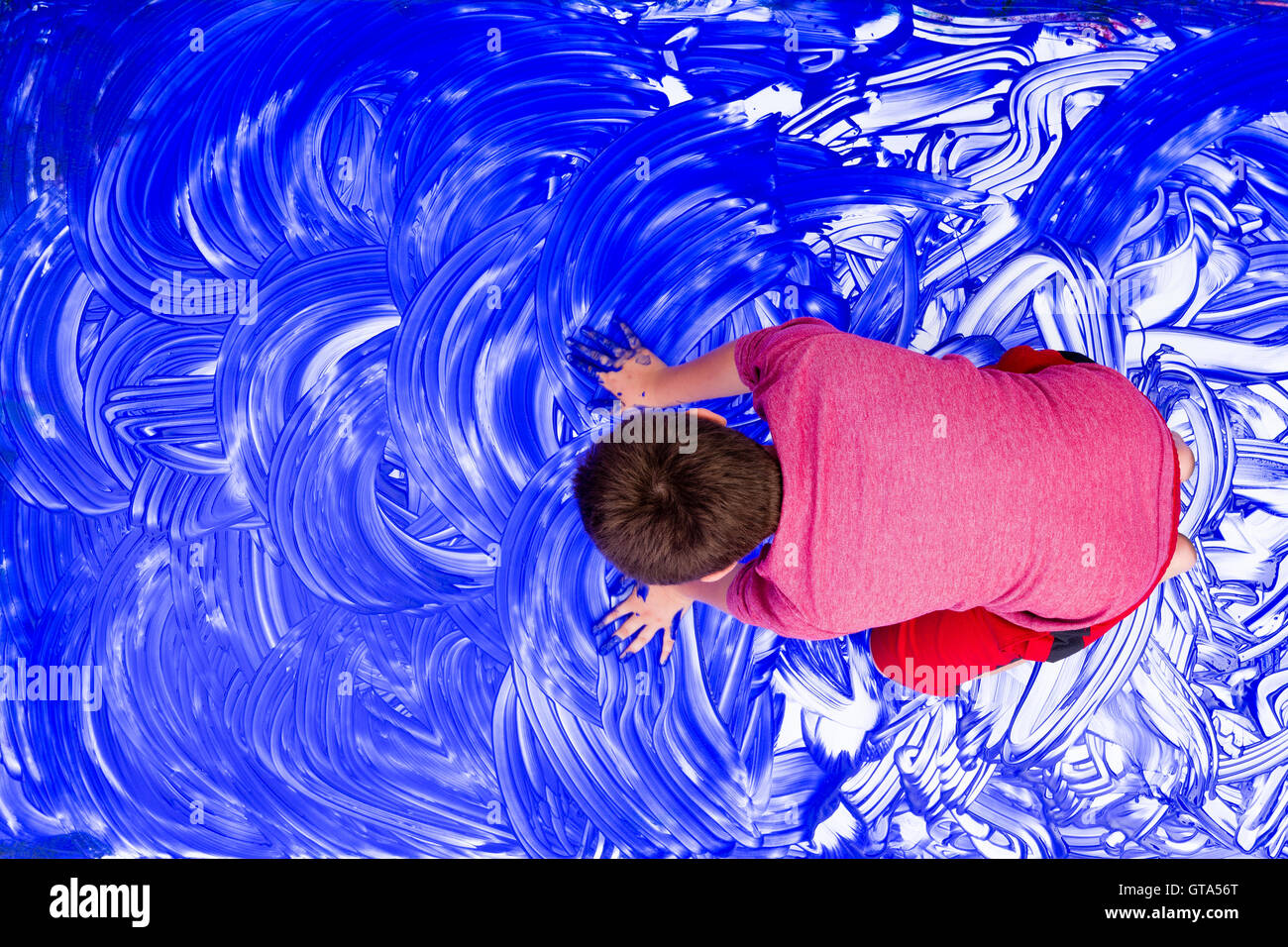 Top-down Ansicht auf jungen Verschmieren Hände in blauer Farbe über weiße Leinwand Papier auf Boden Stockfoto