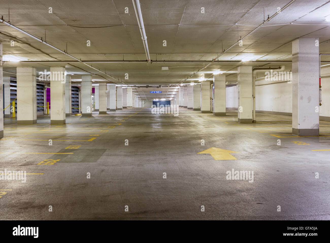 Eingang zum einen trashigen leer überdachten Parkplatz mit einem gelben Pfeil nach vorne auf th durch obenliegende Lichtleisten beleuchtet Stockfoto