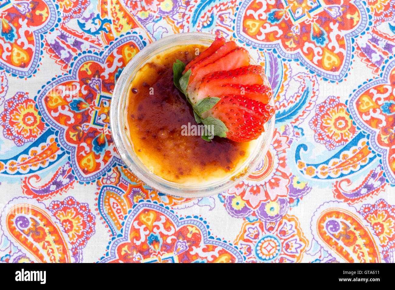 Leckeren Schüssel mit Crème brûlée mit frischen Erdbeeren auf paisley Tisch platziert, wie aus einer Draufsicht zu sehen Stockfoto
