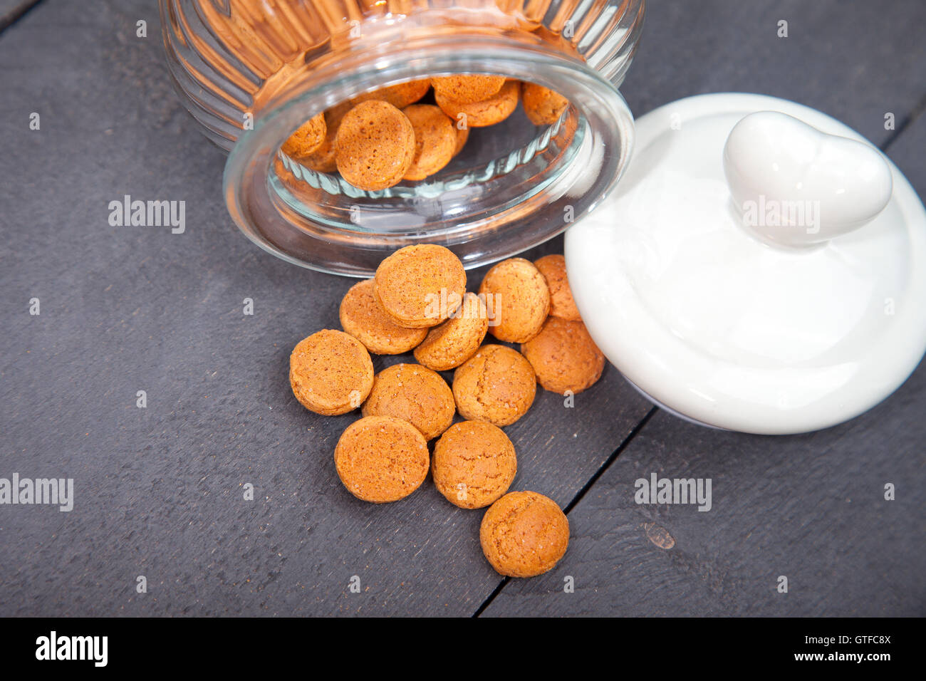 Kleine Haufen von traditionellen niederländischen Süßigkeiten Pepernoten mit Glasabdeckung Jar und Herzen auf schwarzem Hintergrund aus Holz Stockfoto