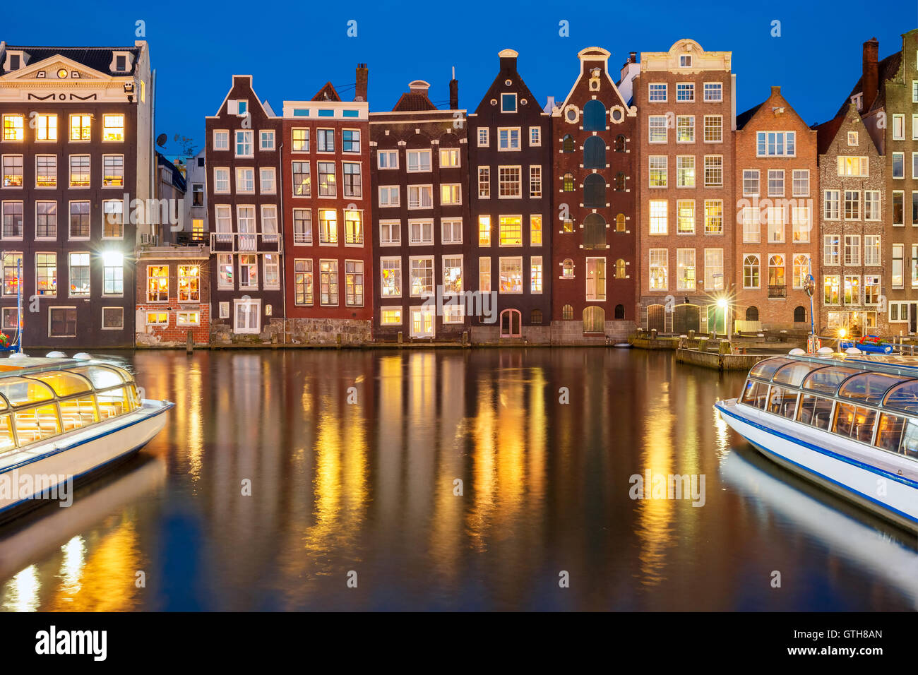 In die Nacht tanzen Häuser am Amsterdamer Kanal Damrak, Holland, Niederlande. Stockfoto