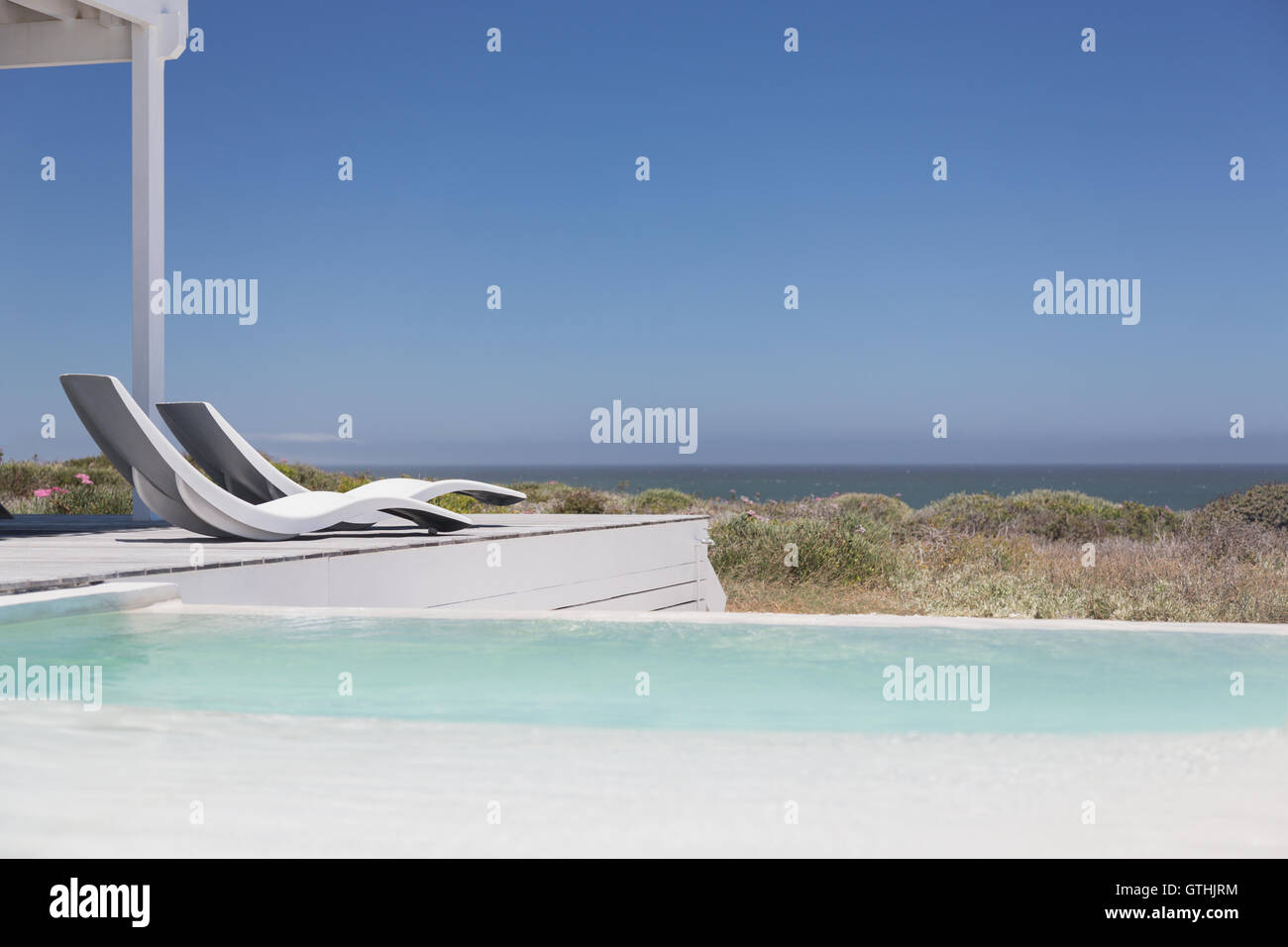 Swimming Pool und modernen Liegestühlen mit Blick auf das Meer unter sonnigen blauen Himmel Stockfoto