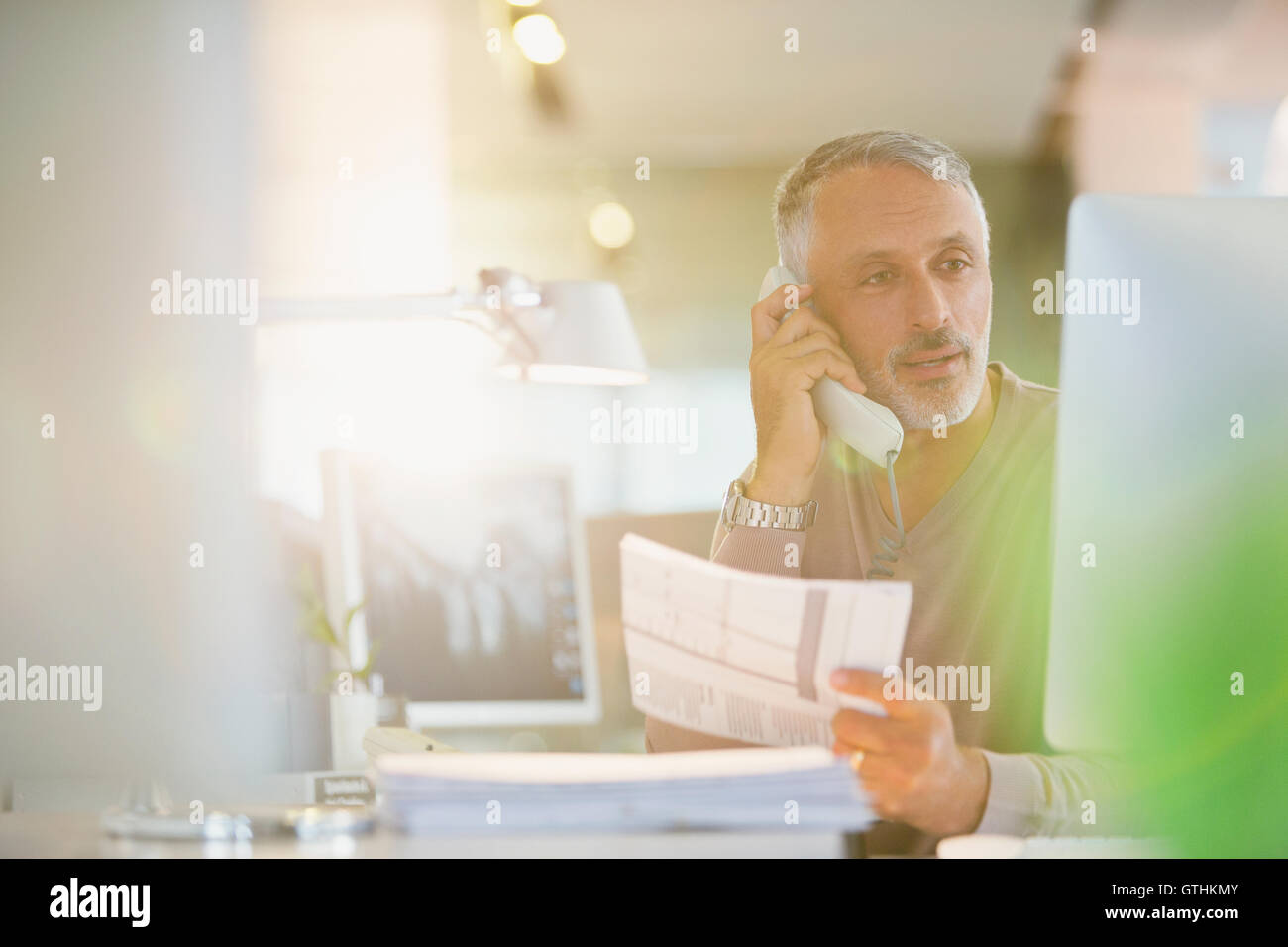 Geschäftsmann mit Papierkram am Computer im Büro am Telefon sprechen Stockfoto