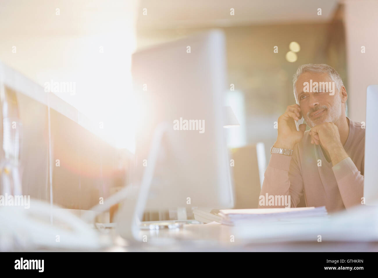 Geschäftsmann, reden über Handy an Computer im sonnigen Büro Stockfoto