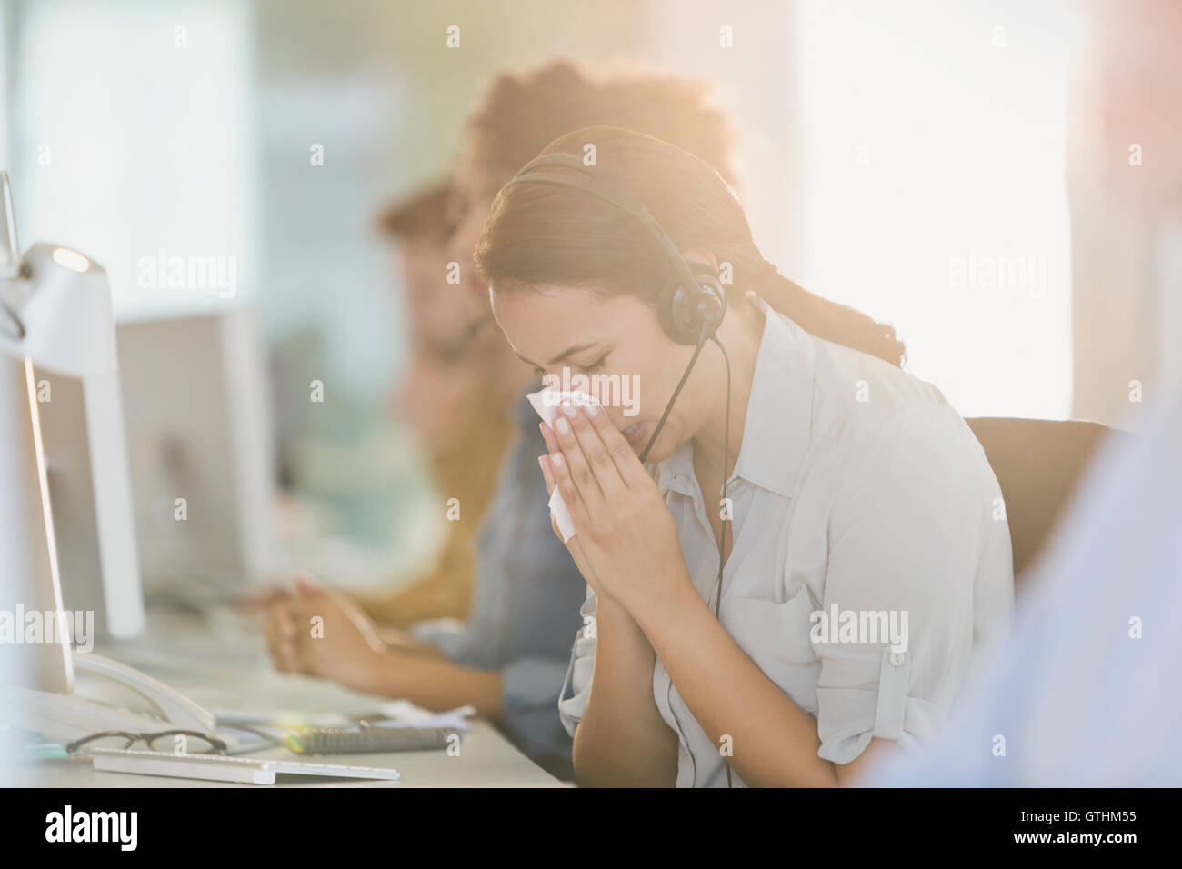 Geschäftsfrau mit Kopfhörer, die Nase weht, am Computer arbeiten Stockfoto