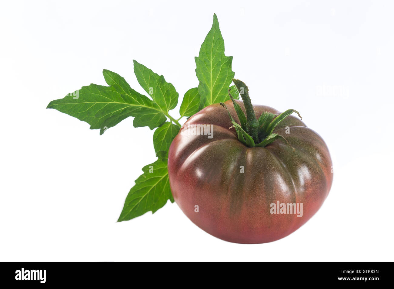 eine isolierte dunkel rote Erbstück-Tomaten mit Blatt Stockfoto