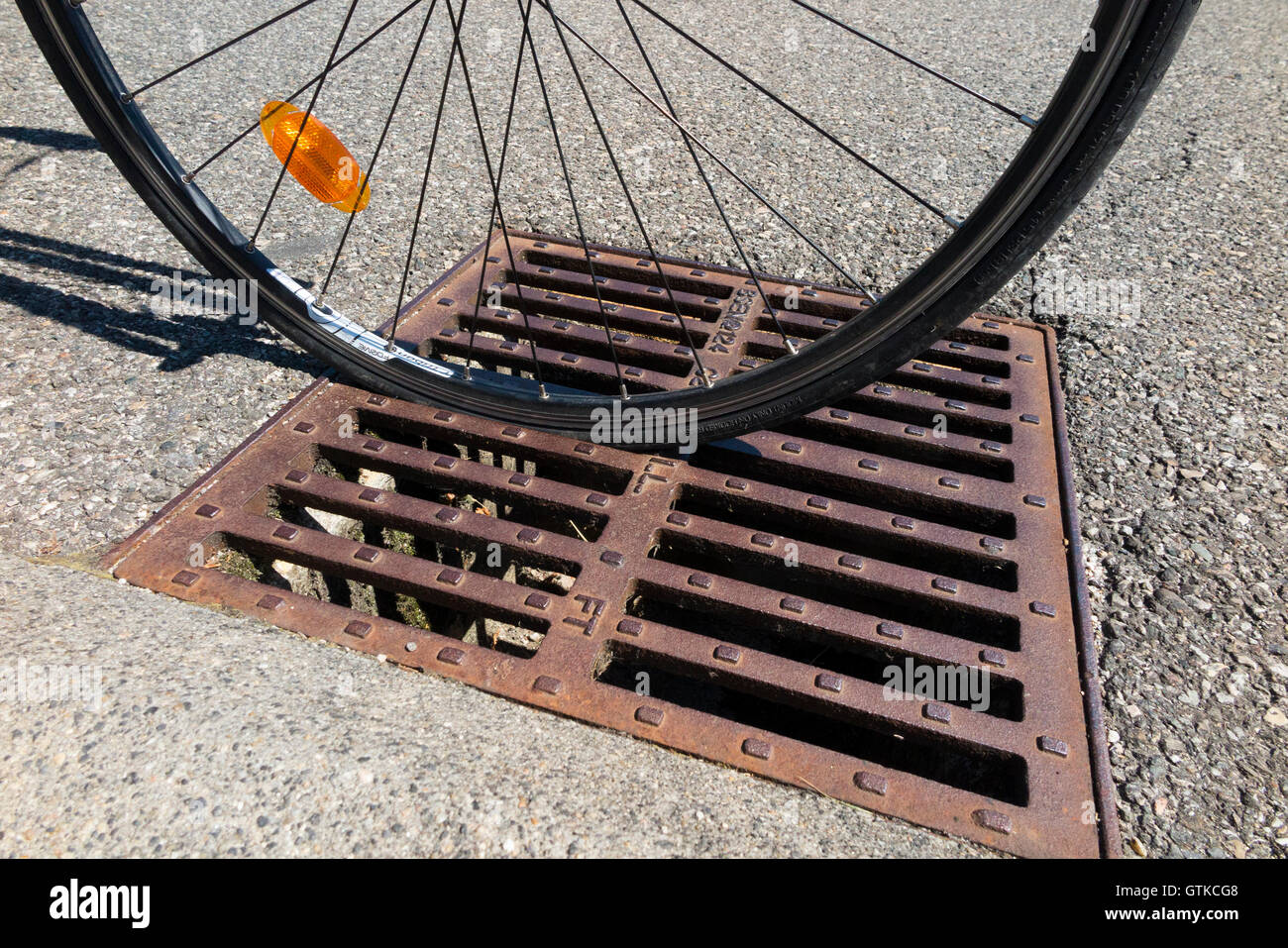Rennrad Fahrrad fahren Rad das gesteckt hat in ein Abfluss Gitter Eisen Cover mit Schlitze in die Richtung der Rinne platziert. Stockfoto