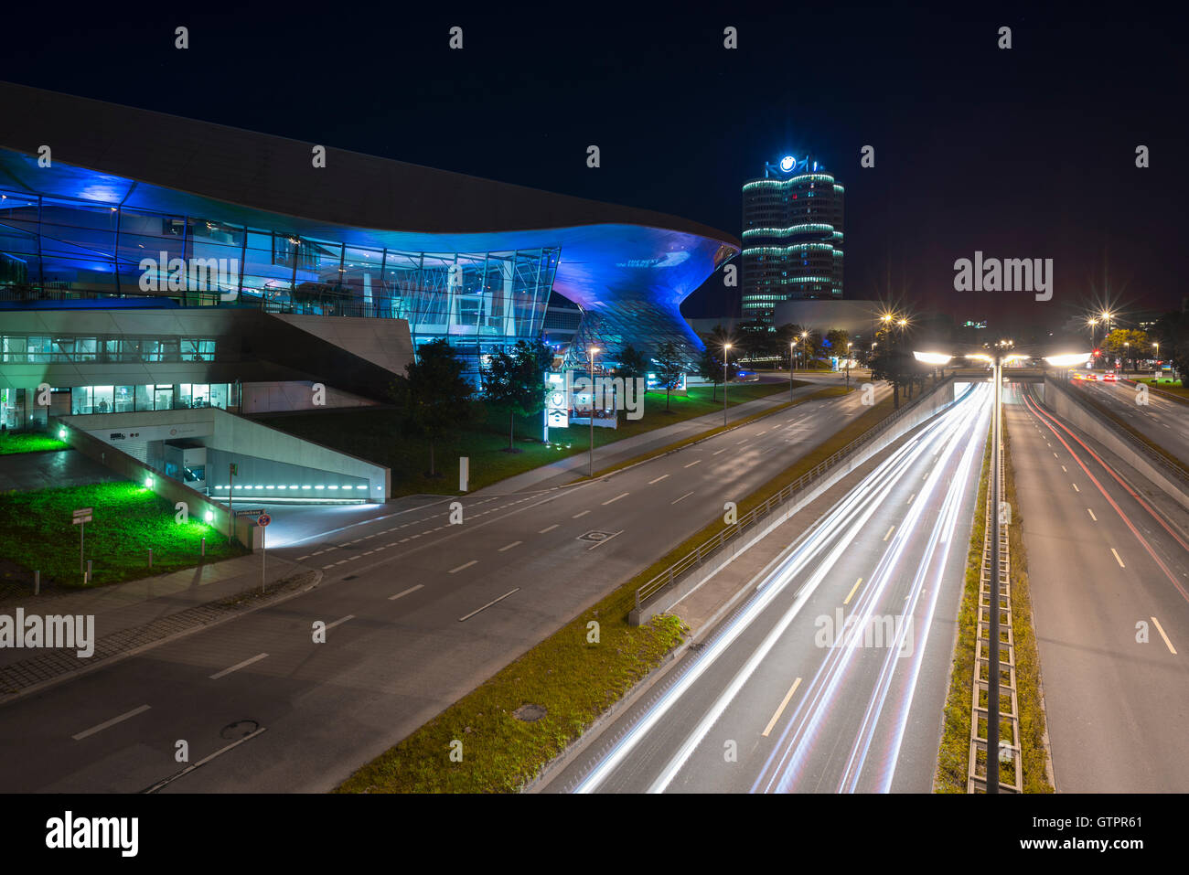 Beleuchtete Fassade der Gebäude der BMW Welt und BMW Hauptsitz mit Verkehr Trails in München in der Nacht, Bayern, Deutschland Stockfoto