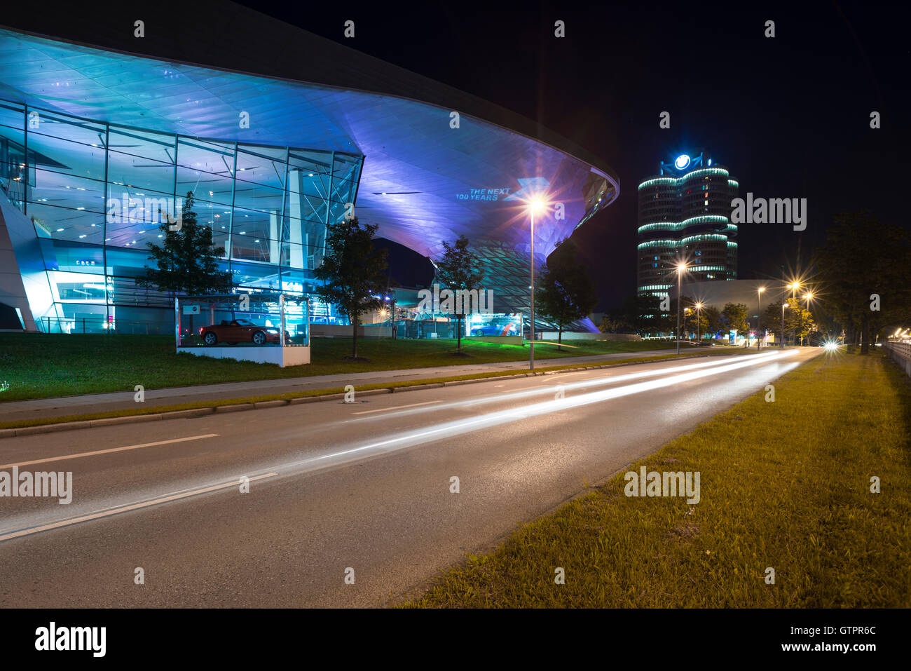 Beleuchtete Fassade der Gebäude der BMW Welt und BMW Hauptsitz mit Verkehr Trails in München in der Nacht, Bayern, Deutschland Stockfoto