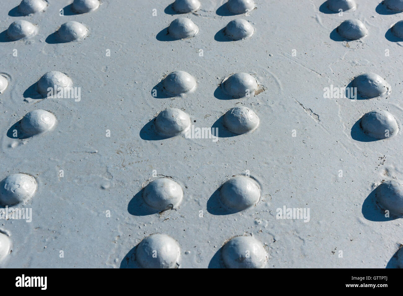 Sonnendurchflutetes grau lackierte Metalloberfläche mit mehreren Reihen von Nietköpfen Stockfoto