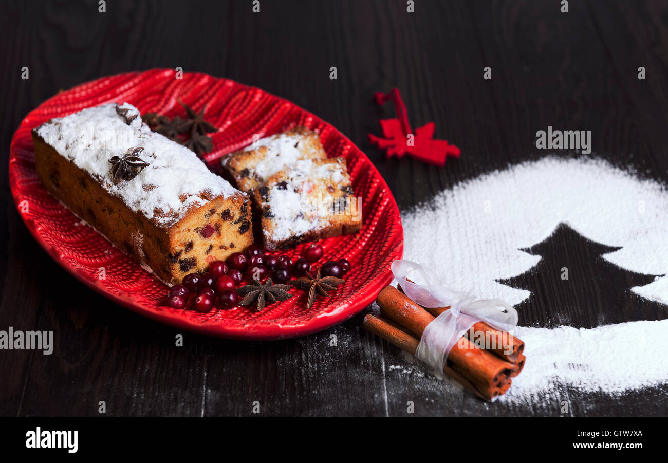 Auf einem hölzernen Schreibtisch-Hintergrund Christstollen, Angel, Puderzucker Angel, eine rote Schale mit Häkelmuster, wie Schnee, Zimt Stockfoto