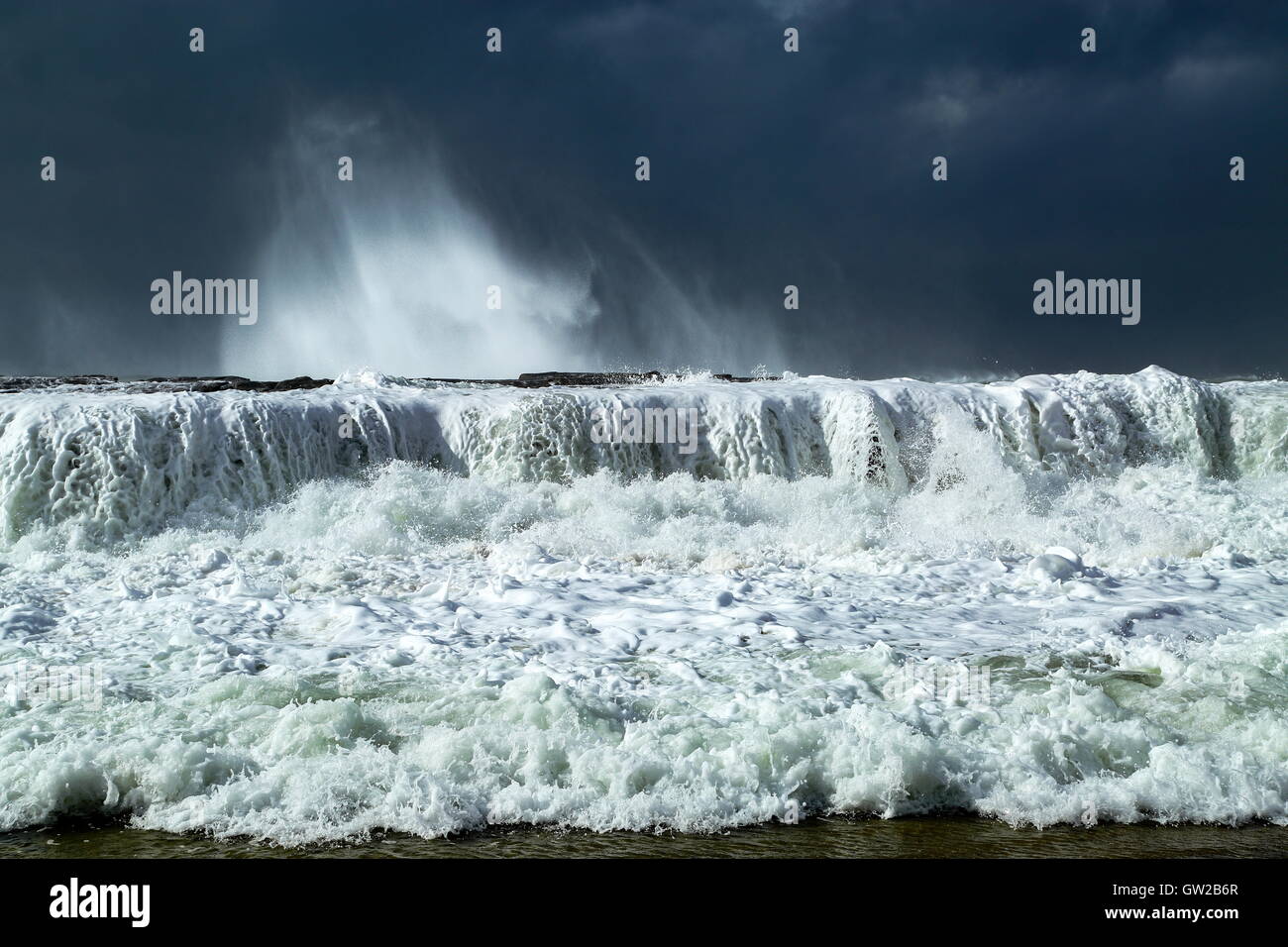 Ein Wintersturm peitscht große und mächtige Wellen, die gegen eine Landzunge, unter einem schweren Himmel abstürzen. Stockfoto