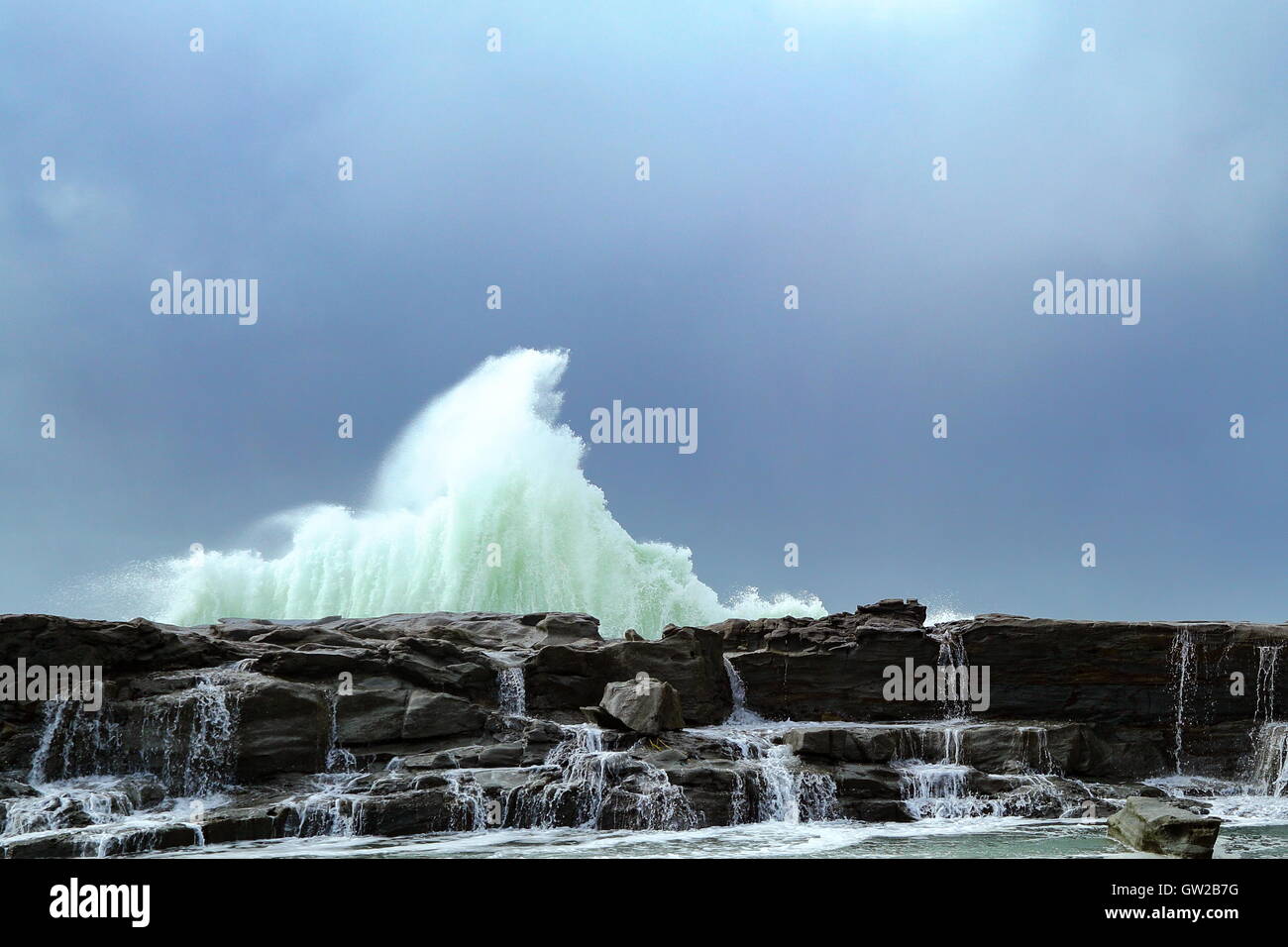 Ein Wintersturm peitscht große und mächtige Wellen, die gegen eine Landzunge, unter einem schweren Himmel abstürzen. Stockfoto