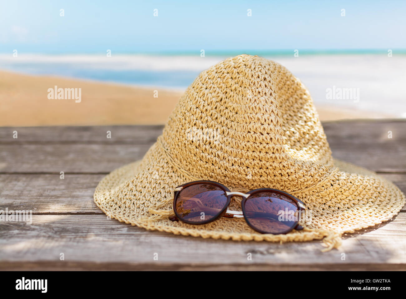 Fedora-Hut und Sonnenbrille auf Holztisch und Meer Landschaft Hintergrund. Stockfoto