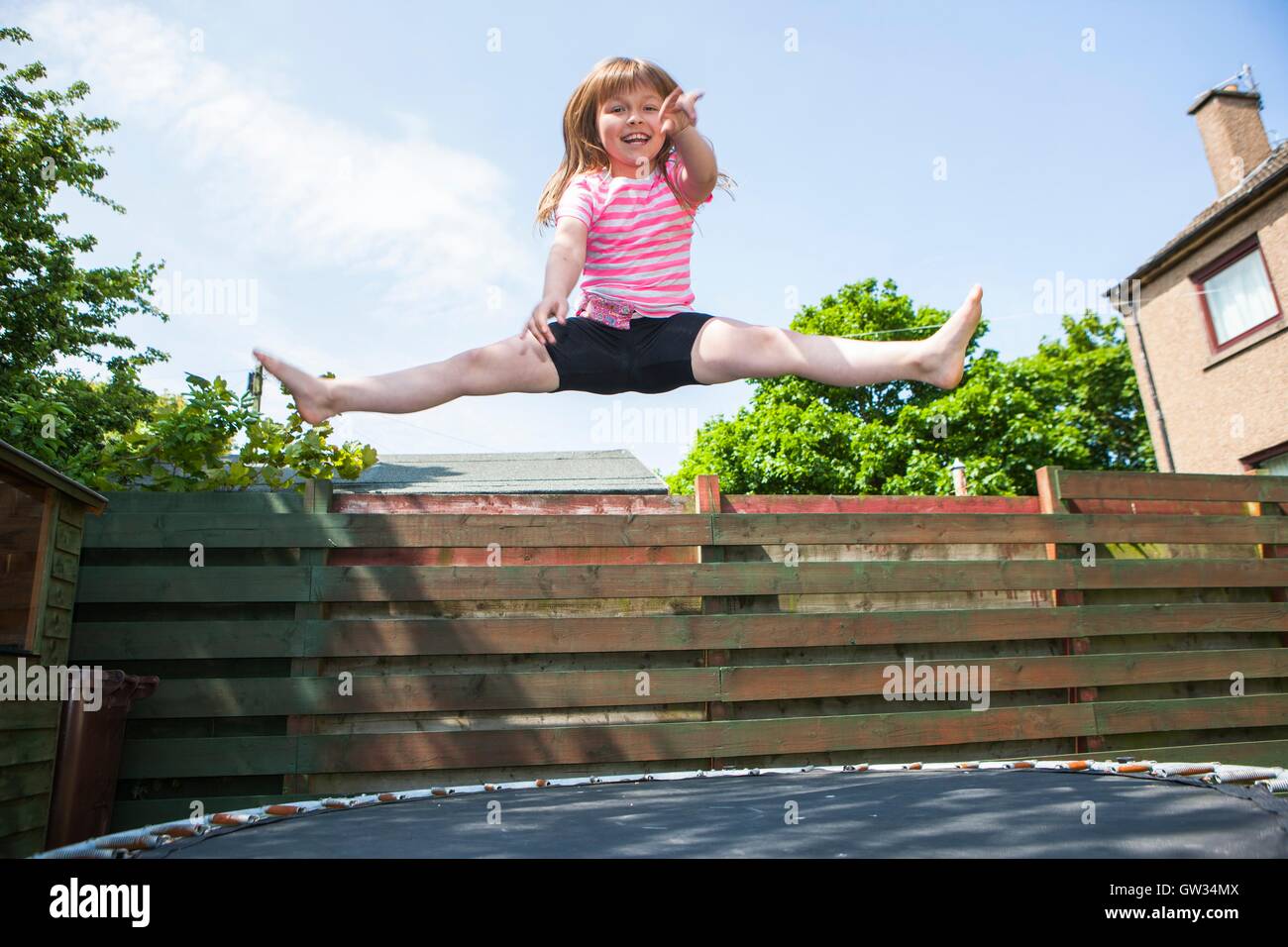 -MODELL VERÖFFENTLICHT. Junges Mädchen auf dem Trampolin. 8 Jahre altes Mädchen springen in der Luft während des Spielens auf einem Trampolin im Garten. Stockfoto