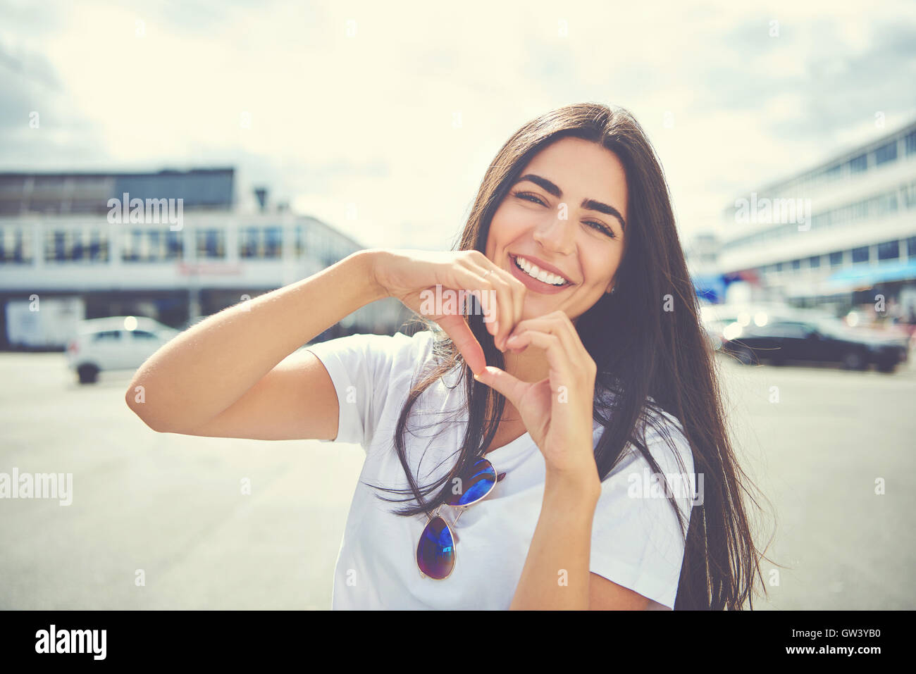 Lachen, attraktive junge Frau, die im Freien in einem städtischen Umfeld, ein Herz, das symbolische Geste mit den Händen der Liebe Stockfoto