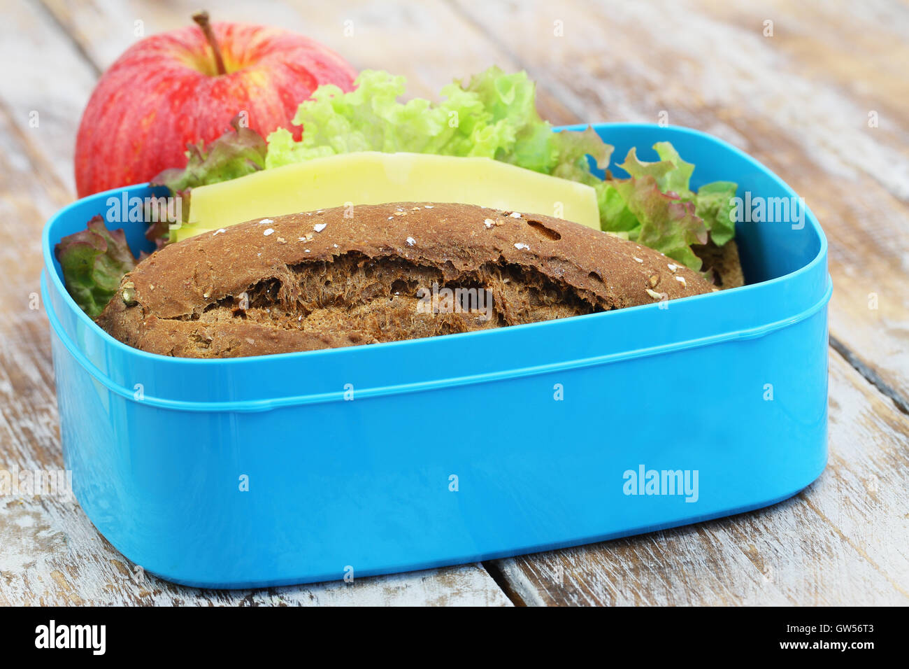 Lunch-Box mit braunen Käse-Sandwich und roter Apfel auf rustikalen Holzoberfläche verpackt Stockfoto