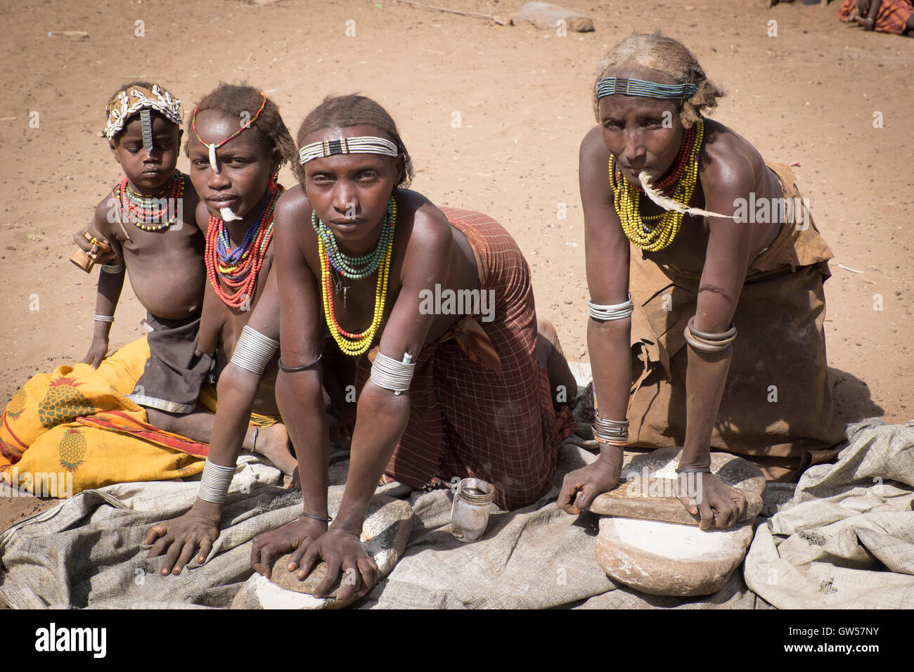 Vier Generationen von den Frauen des Stammes Dasanech im Tal Omo River von Südäthiopien mahlen Sorghum für Lebensmittel Stockfoto