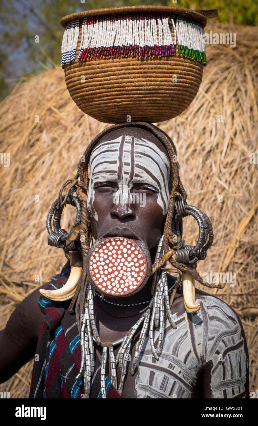 Mursi-Frau das Omo-Tal in Äthiopien mit Mundlochplatte, Körper Malerei, Knochen Ohrringe und Korb Stockfoto