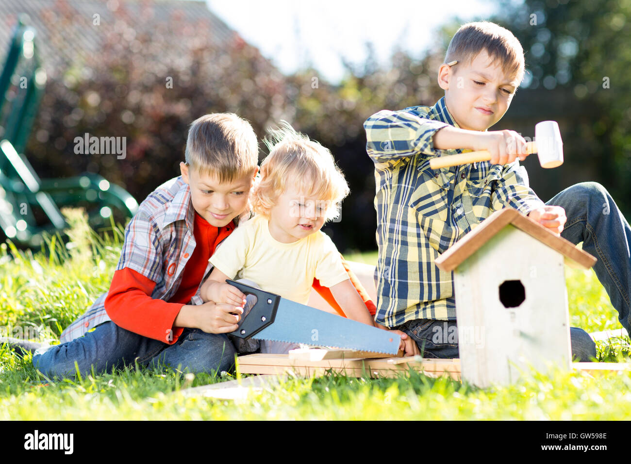 Kinder machen Vogelhaus zusammen sitzen auf dem Rasen. Ältestes Kind lehrt jüngsten Bruder mit Werkzeugen arbeiten Stockfoto