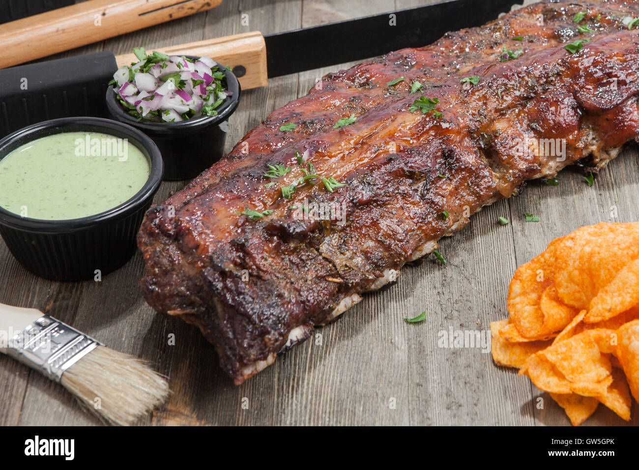 Baby zurück ribs auf einem Holz dienen Board begleitet von frischer Koriander Sauce Bbq gebacken-Chips, rote Zwiebeln und Koriander schneiden Stockfoto