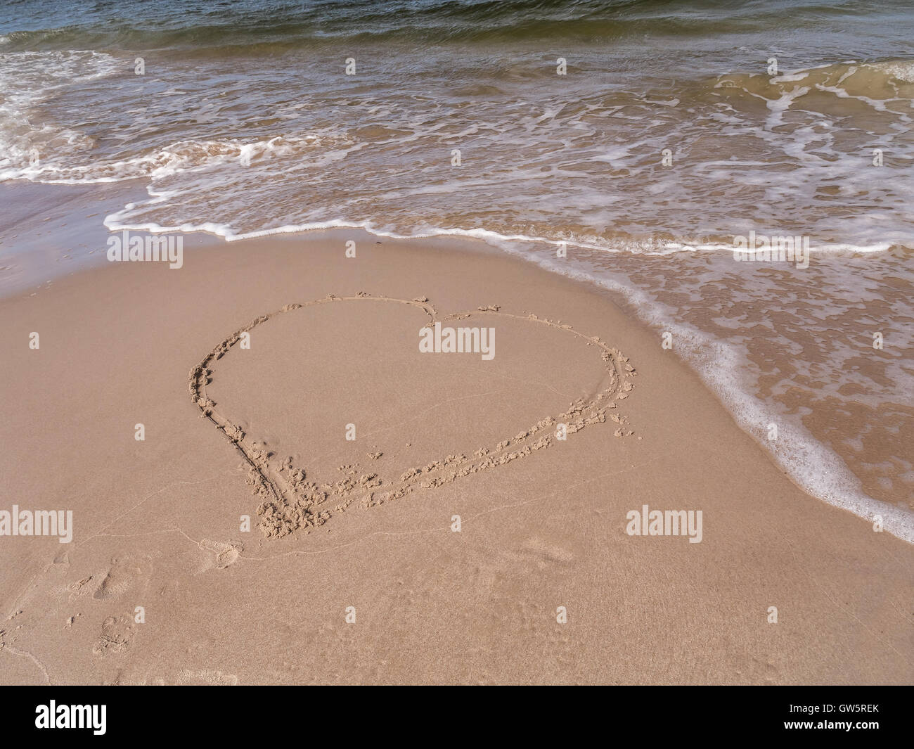 Handgezeichnete Herz am Sandstrand mit der nächsten Welle Stockfoto