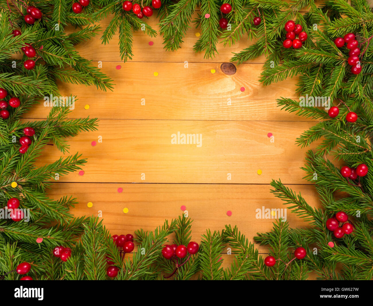 Weihnachtsbaum und rote Beeren-Frame auf den Holzplanken Hintergrund mit roten und gelben Konfetti bestreut Stockfoto