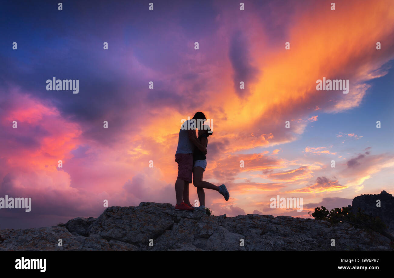 Landschaft mit Silhouetten von einem umarmen und küssen Mann und Freundin auf der Bergspitze an farbenprächtigen Sonnenuntergang Stockfoto